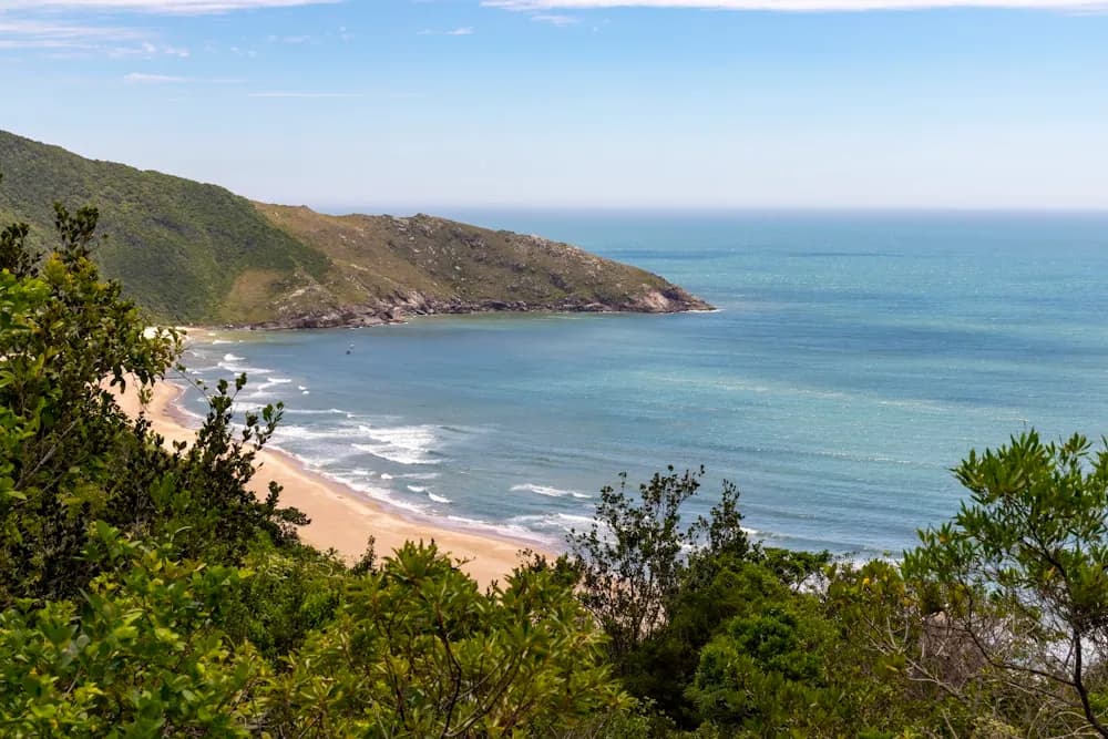 Praia vista do alto de um morro, com o mar aberto ao fundo