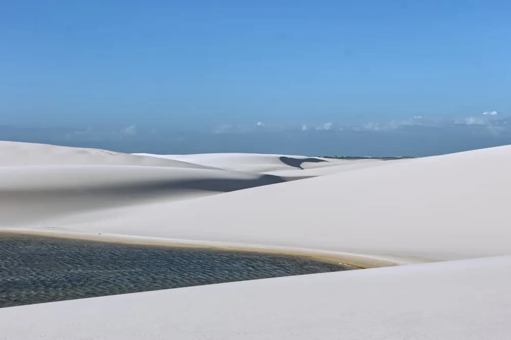 Dunas de areia branca com uma lagoa azul entre elas